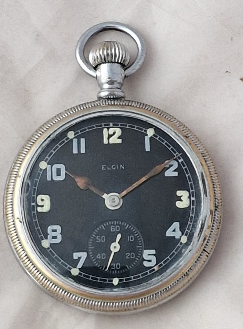 An Elgin military pocket watch with a black dial, luminous Arabic numerals, a sub-seconds dial, and a silver-tone metal case.