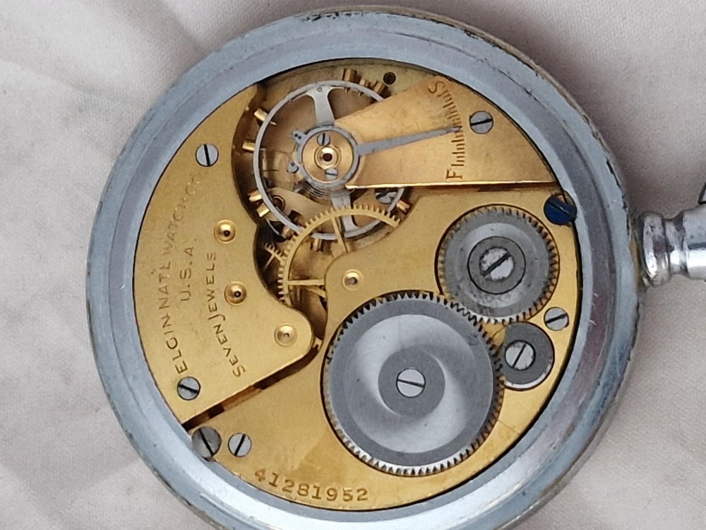 An Elgin military pocket watch with a black dial, luminous Arabic numerals, a sub-seconds dial, and a silver-tone metal case. View III