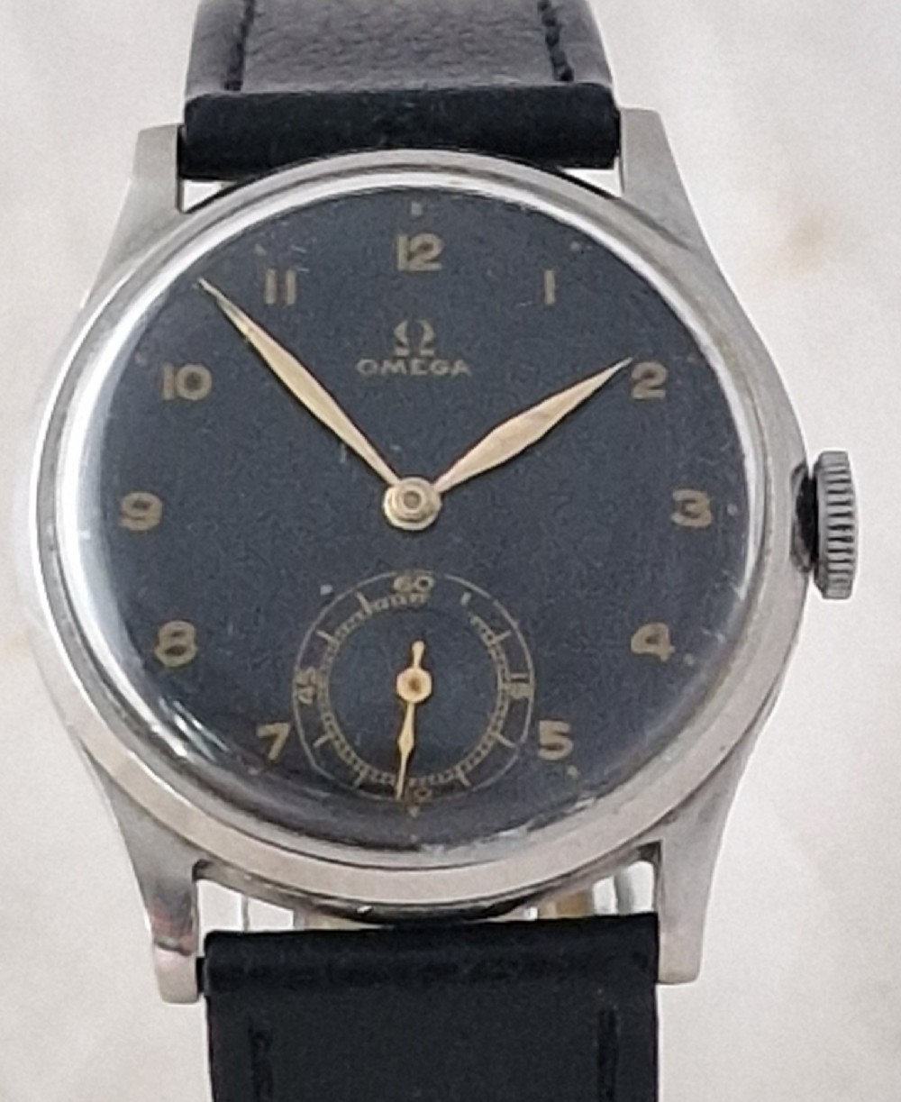 A vintage 1944 Omega wristwatch featuring a circular stainless steel case, black dial with Arabic numerals, sub-seconds dial, and a black leather strap.