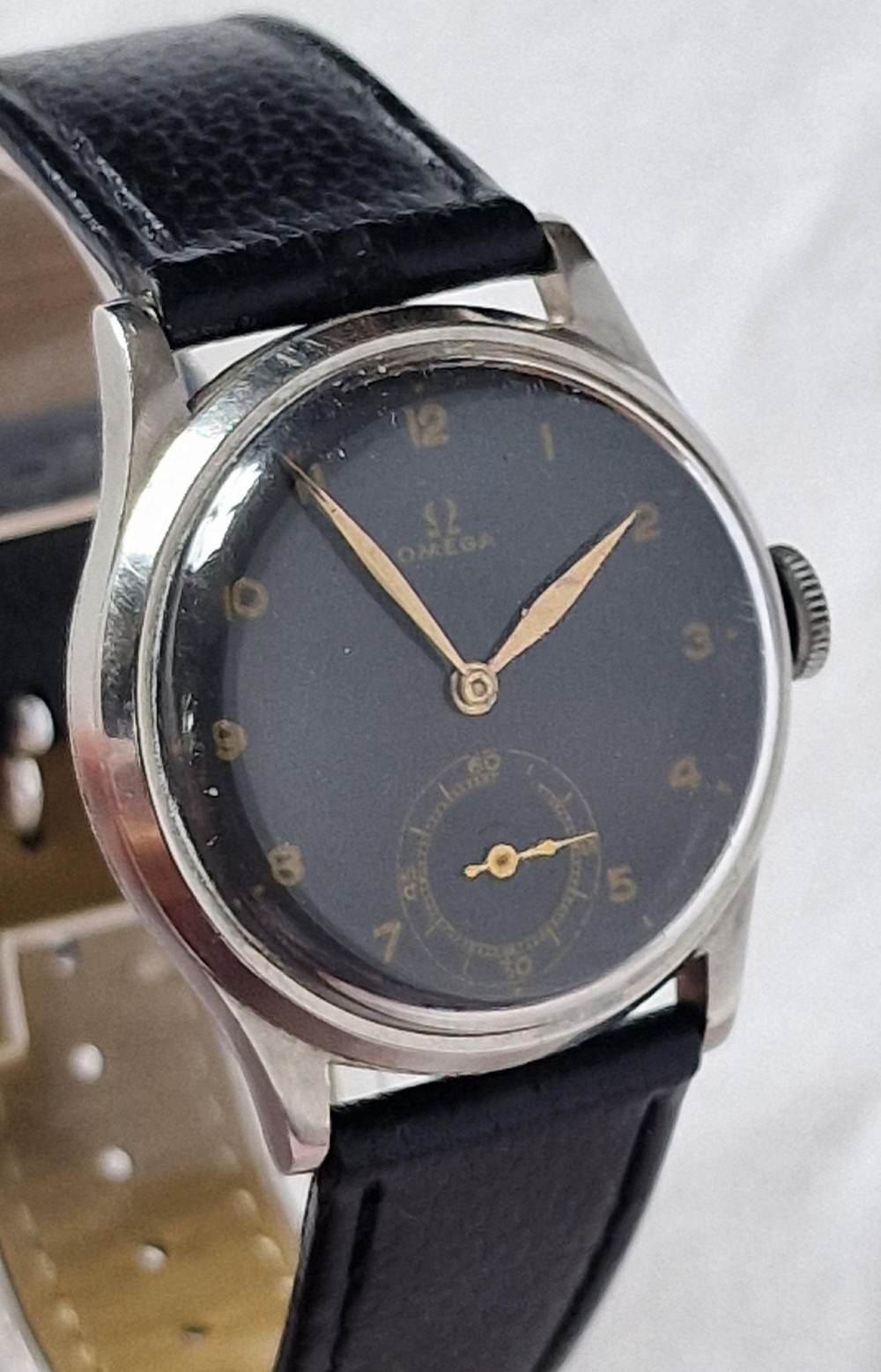 A vintage 1944 Omega wristwatch featuring a circular stainless steel case, black dial with Arabic numerals, sub-seconds dial, and a black leather strap. View III