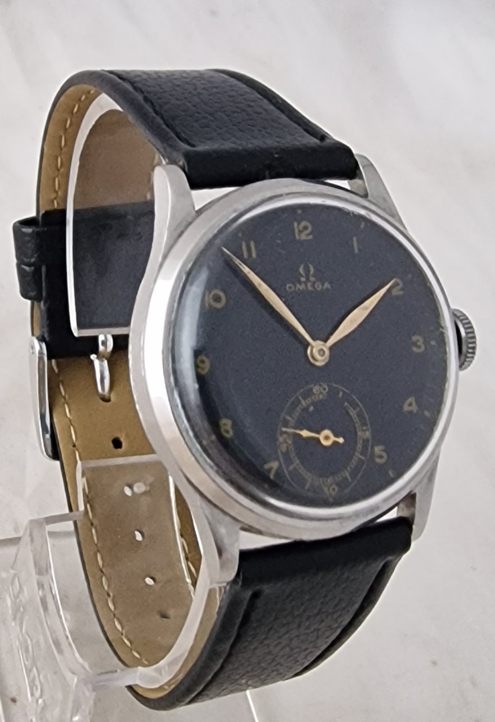 A vintage 1944 Omega wristwatch featuring a circular stainless steel case, black dial with Arabic numerals, sub-seconds dial, and a black leather strap. View IV