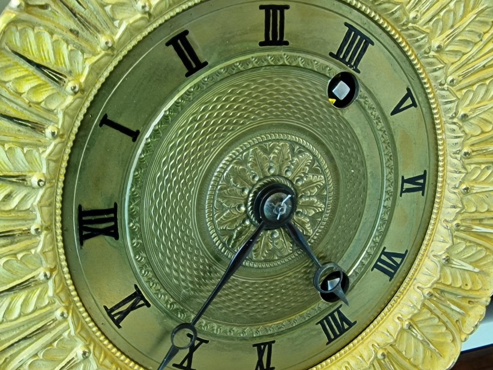 An antique French Empire portico clock featuring four mahogany columns with ornate gilt bronze capitals, an exposed decorative pendulum, and a gilded dial set within a mahogany framework. View III