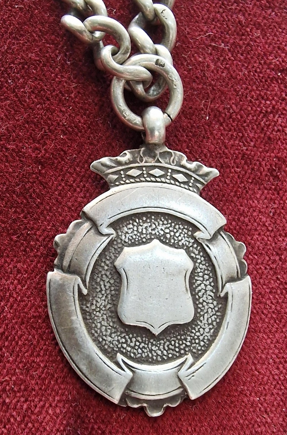 An antique silver pocket watch chain featuring curb links, a swivel clasp, a bolt ring, and a suspended crown-topped shield fob. View III