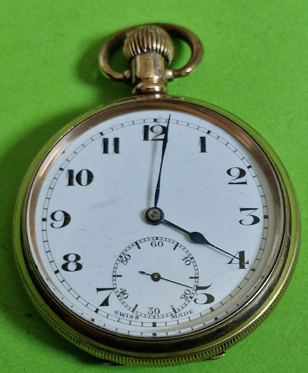 An open-face gold-toned pocket watch featuring a white enamel dial with black Arabic numerals, blued steel hands, and a subsidiary seconds sub-dial at six oclock.