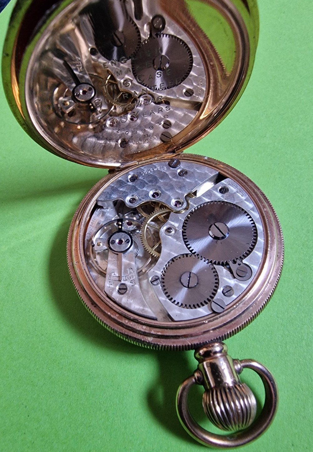An open-face gold-toned pocket watch featuring a white enamel dial with black Arabic numerals, blued steel hands, and a subsidiary seconds sub-dial at six oclock. View V