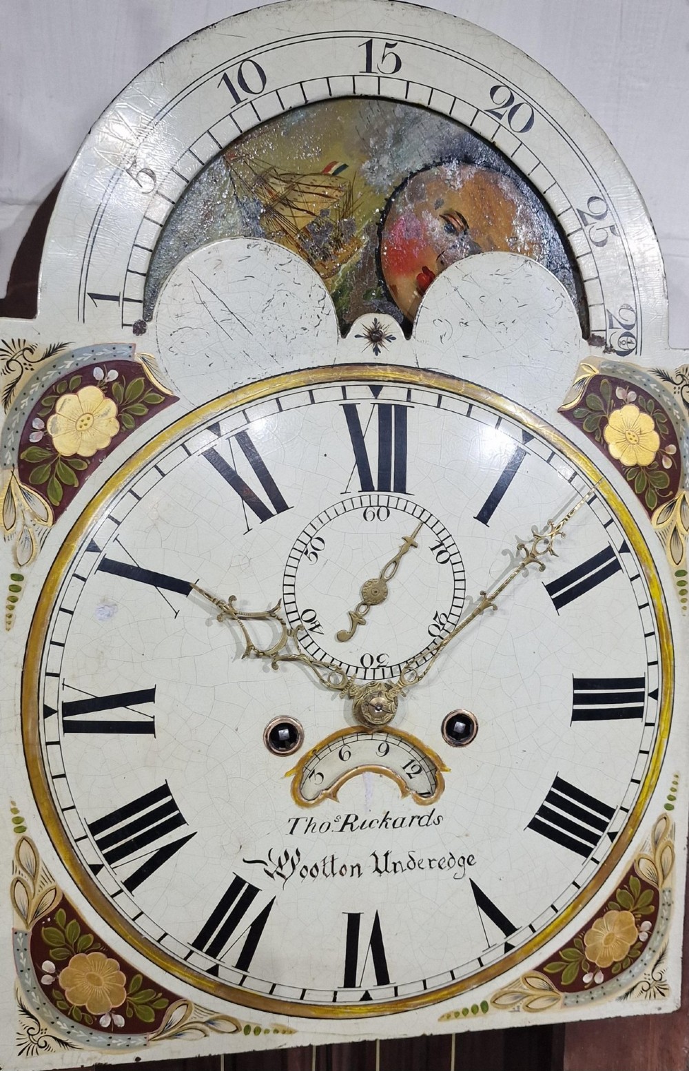 An antique Georgian flame mahogany longcase clock with three brass finials, an arched hood, fluted columns, and a painted dial displaying a moonphase mechanism. View IV