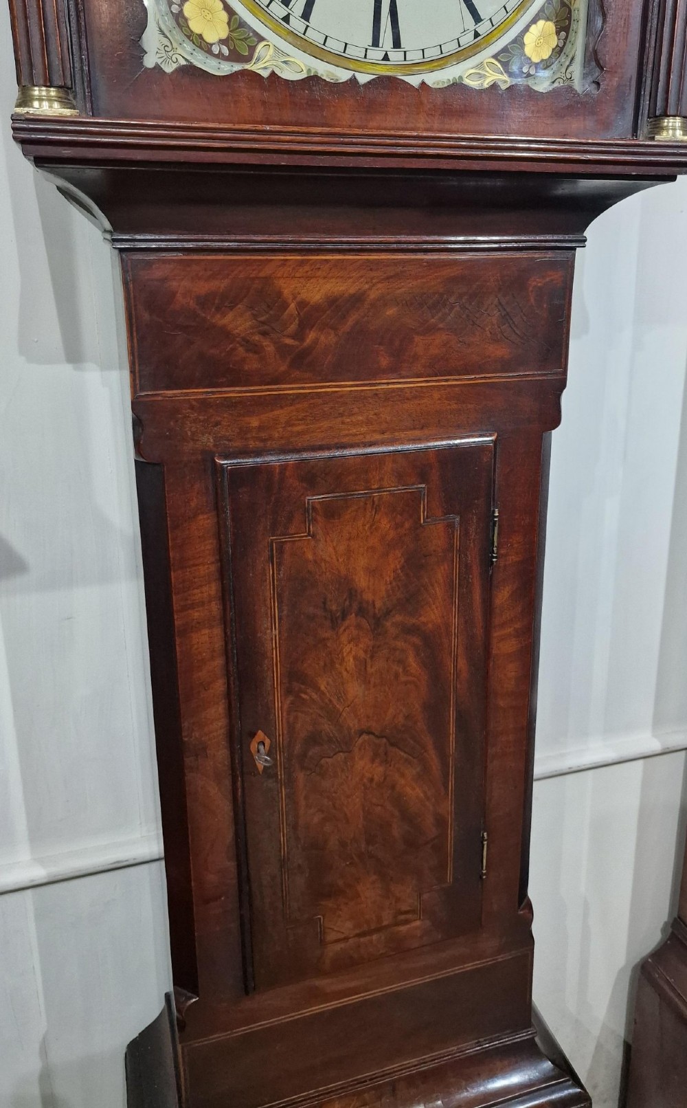 An antique Georgian flame mahogany longcase clock with three brass finials, an arched hood, fluted columns, and a painted dial displaying a moonphase mechanism. View VIII
