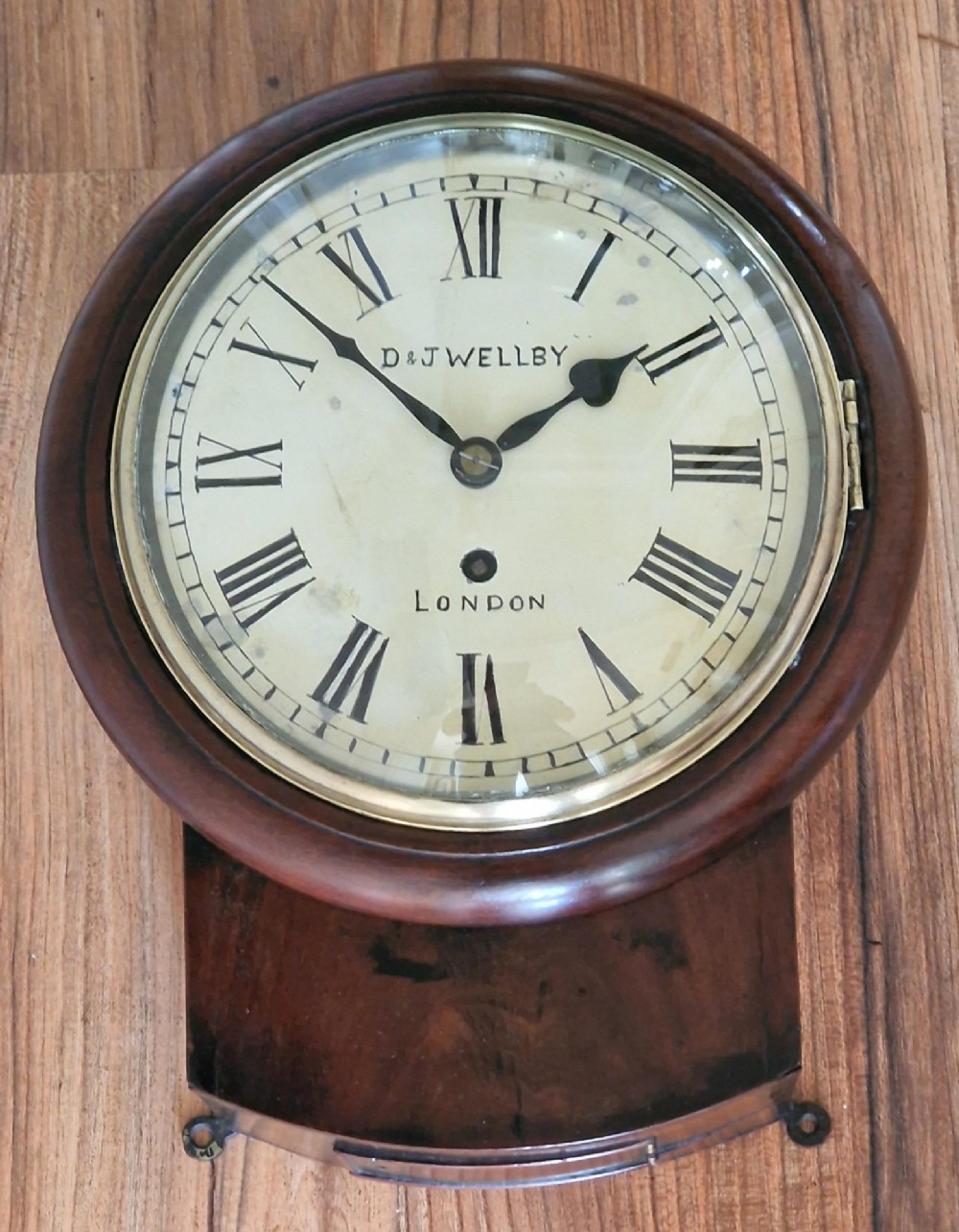A small mahogany fusee wall clock featuring an eight-inch dial with Roman numerals, a brass bezel, and a lower wooden drop case.