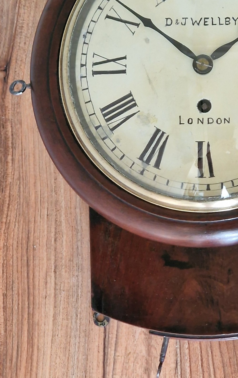 A small mahogany fusee wall clock featuring an eight-inch dial with Roman numerals, a brass bezel, and a lower wooden drop case. View V