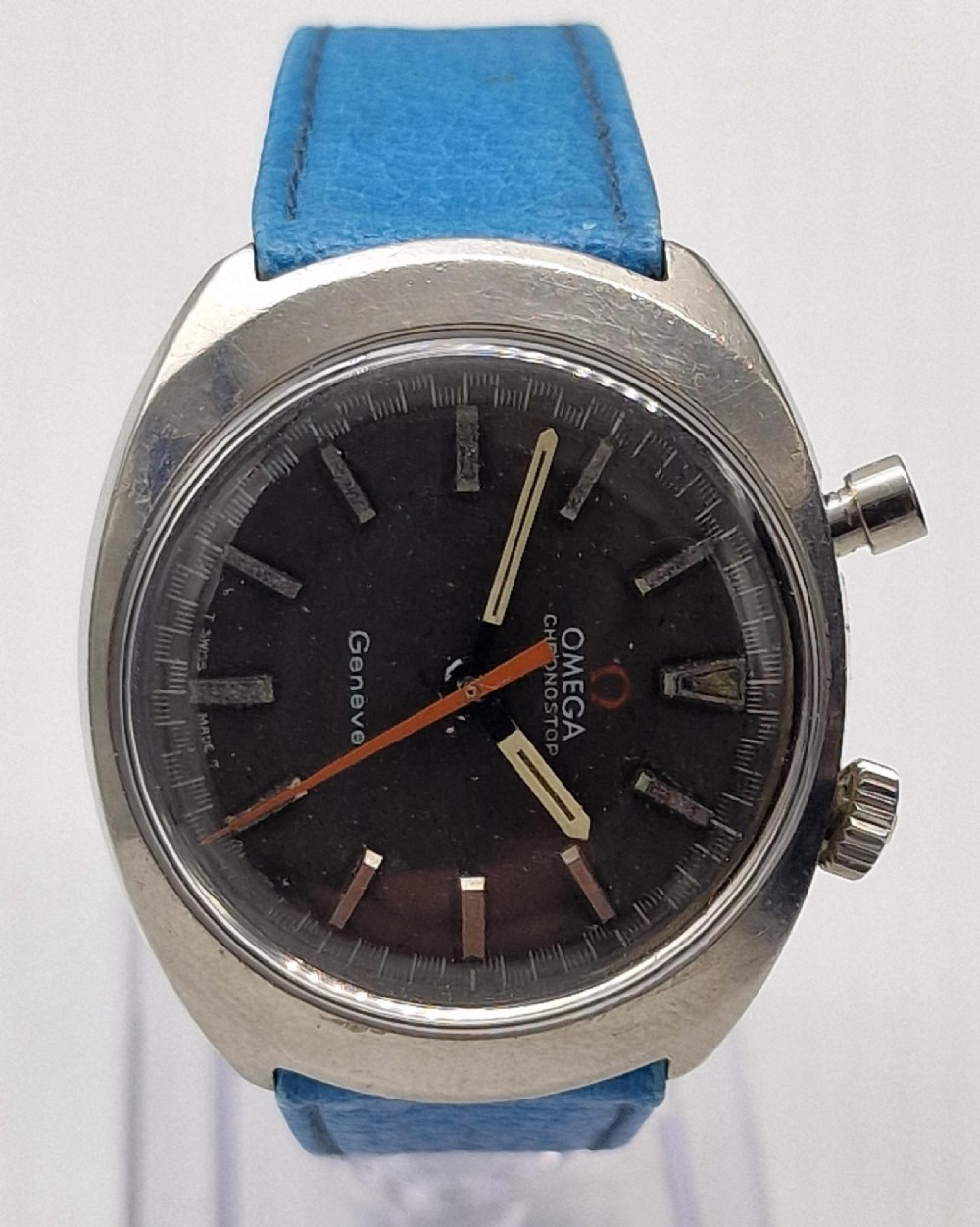 A 1969 Omega Chronostop stainless steel wristwatch featuring a dark dial, an orange seconds hand, and a bright blue leather strap.