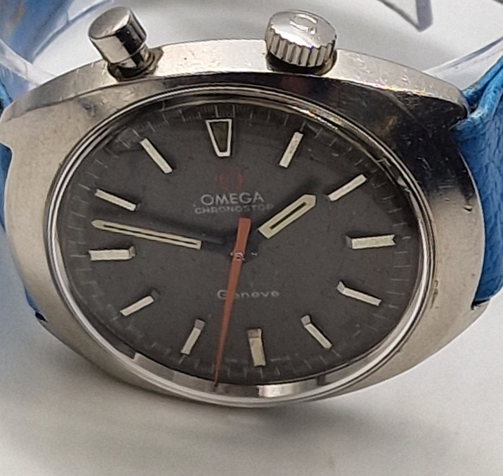 A 1969 Omega Chronostop stainless steel wristwatch featuring a dark dial, an orange seconds hand, and a bright blue leather strap. View II