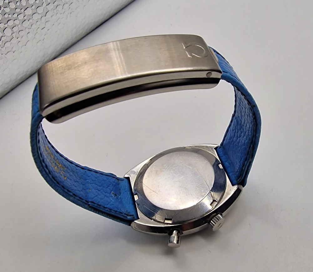 A 1969 Omega Chronostop stainless steel wristwatch featuring a dark dial, an orange seconds hand, and a bright blue leather strap. View III