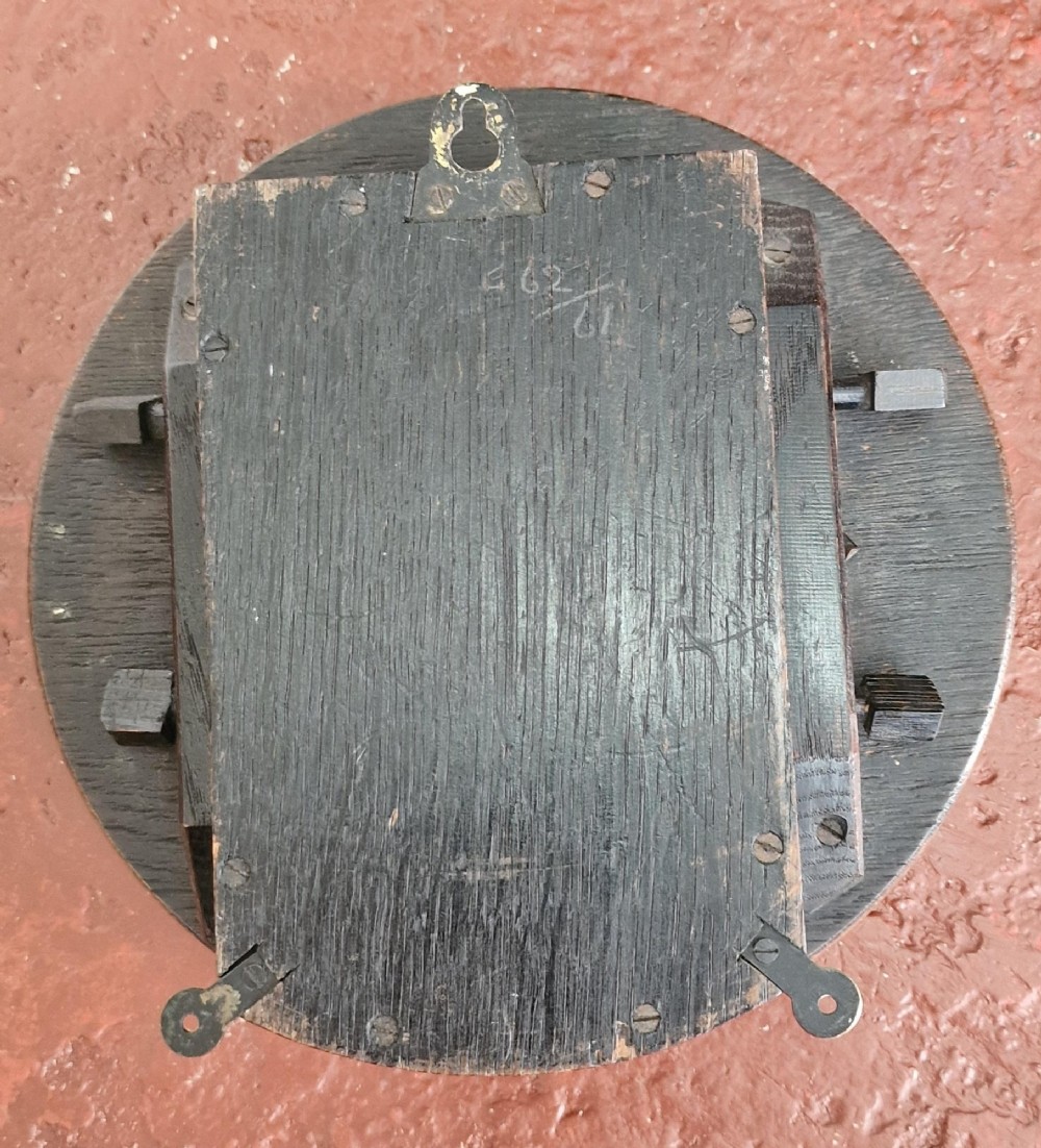 A circular antique oak wall clock featuring a white face with Roman numerals, a brass bezel, and a moulded wood surround. View II