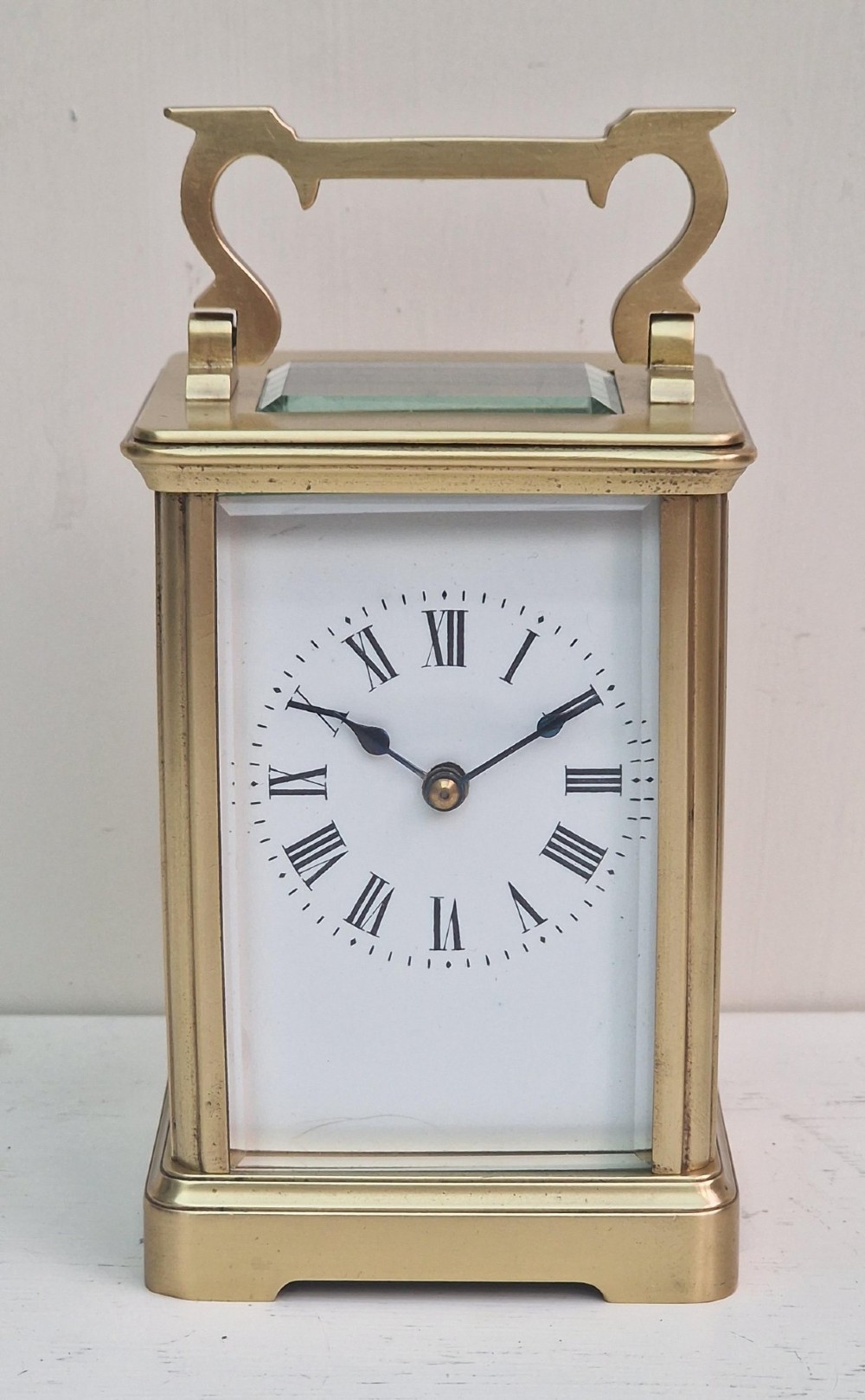 A rectangular brass French carriage clock featuring bevelled glass panels, a white enamel dial with black Roman numerals, and a top carrying handle.