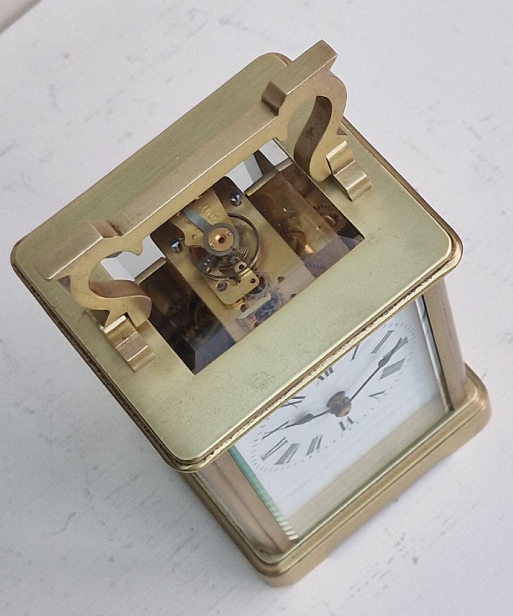A rectangular brass French carriage clock featuring bevelled glass panels, a white enamel dial with black Roman numerals, and a top carrying handle. View II