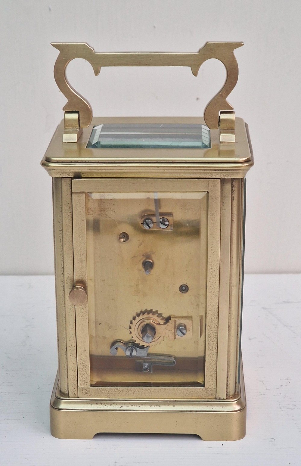 A rectangular brass French carriage clock featuring bevelled glass panels, a white enamel dial with black Roman numerals, and a top carrying handle. View III