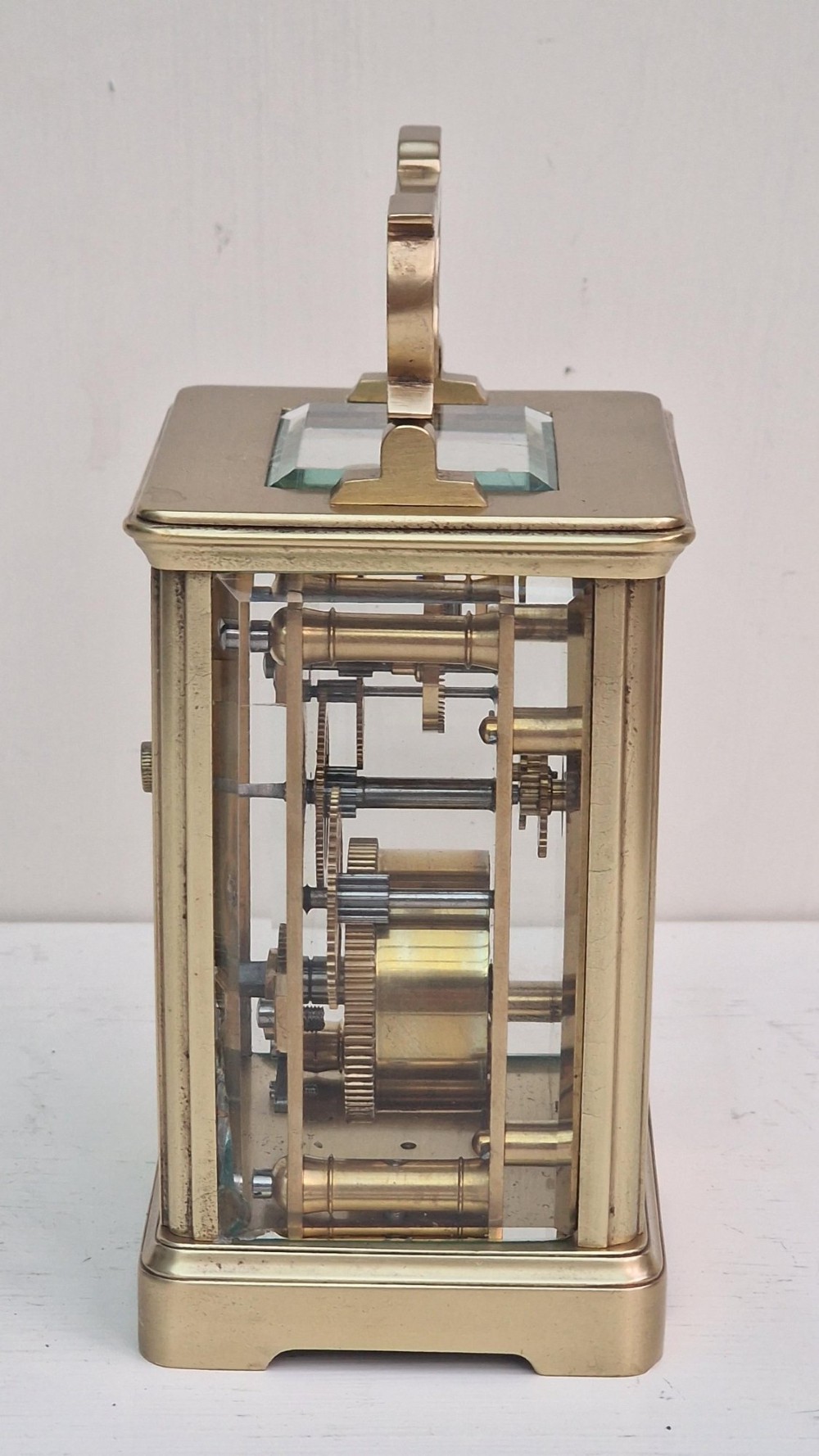 A rectangular brass French carriage clock featuring bevelled glass panels, a white enamel dial with black Roman numerals, and a top carrying handle. View IV