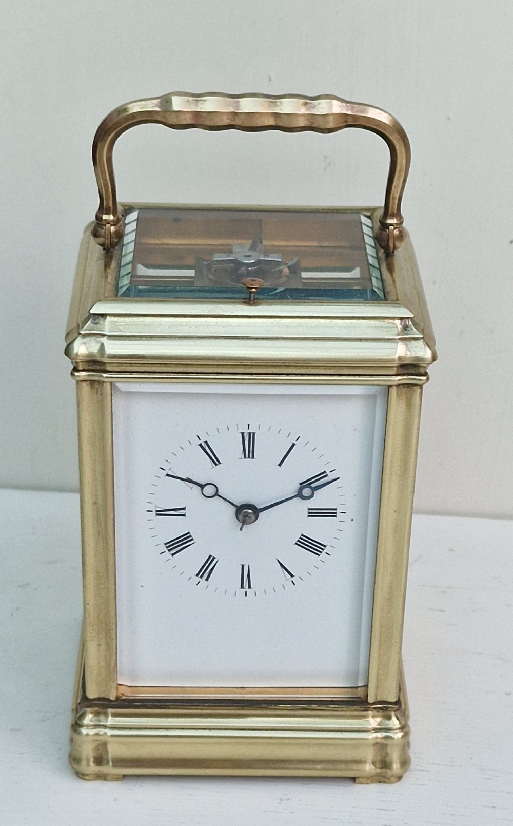 An antique French brass carriage clock featuring a gorge case structure, bevelled glass side panels, a white enamel dial with Roman numerals, and a top carrying handle. View II