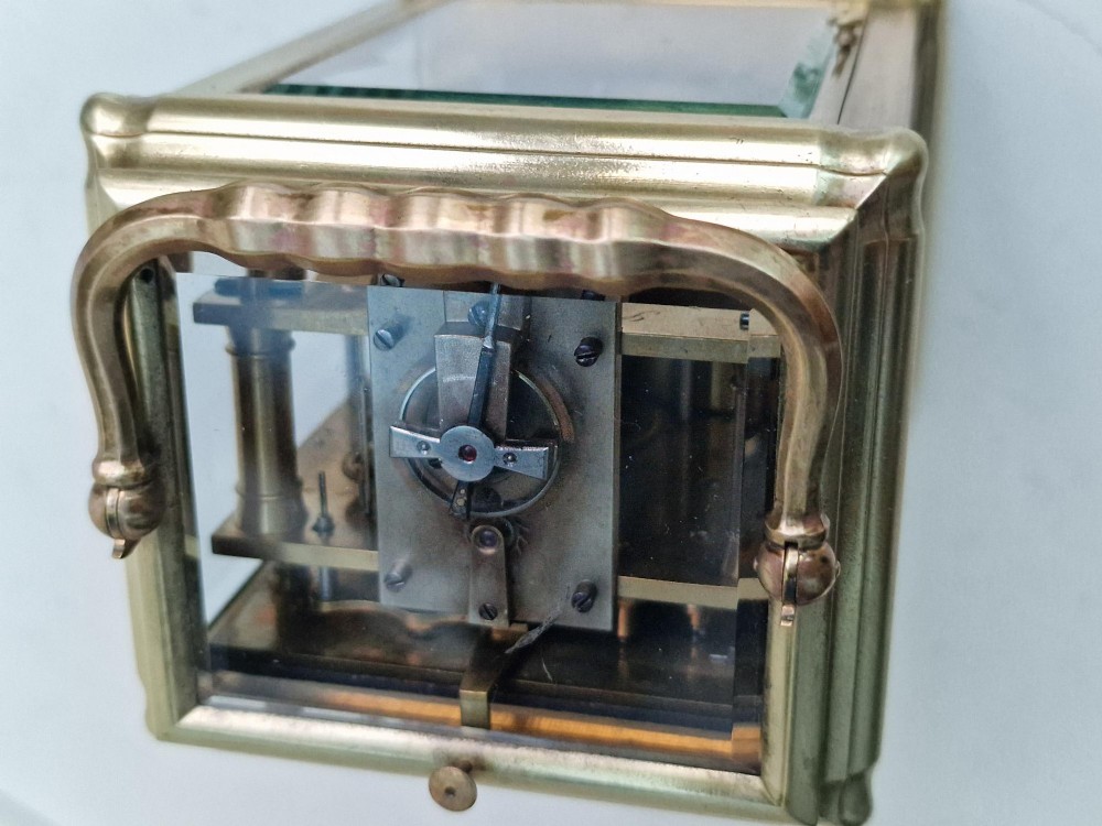 An antique French brass carriage clock featuring a gorge case structure, bevelled glass side panels, a white enamel dial with Roman numerals, and a top carrying handle. View III