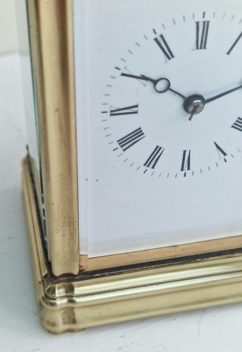 An antique French brass carriage clock featuring a gorge case structure, bevelled glass side panels, a white enamel dial with Roman numerals, and a top carrying handle. View IV