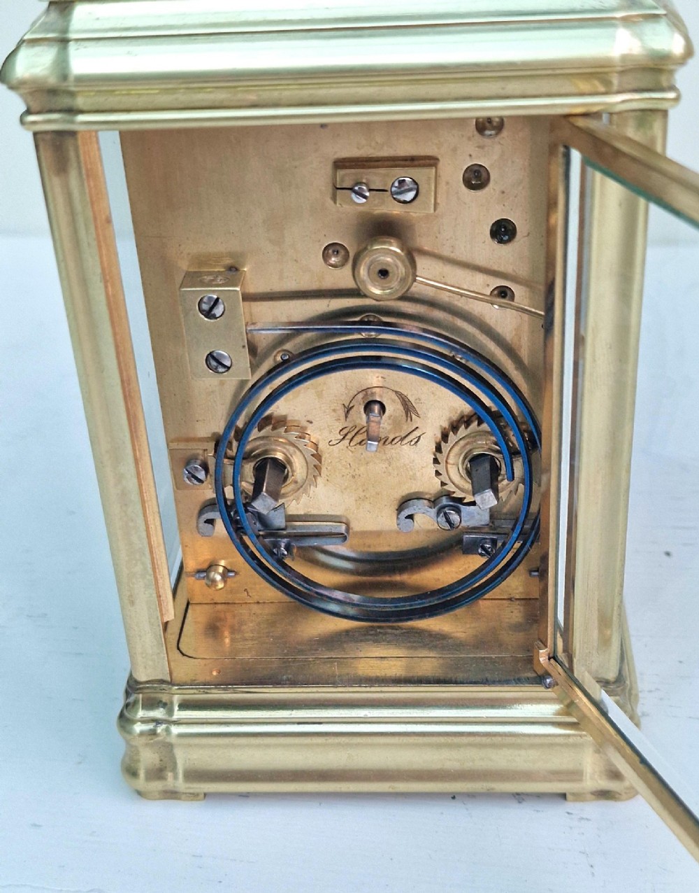 An antique French brass carriage clock featuring a gorge case structure, bevelled glass side panels, a white enamel dial with Roman numerals, and a top carrying handle. View V