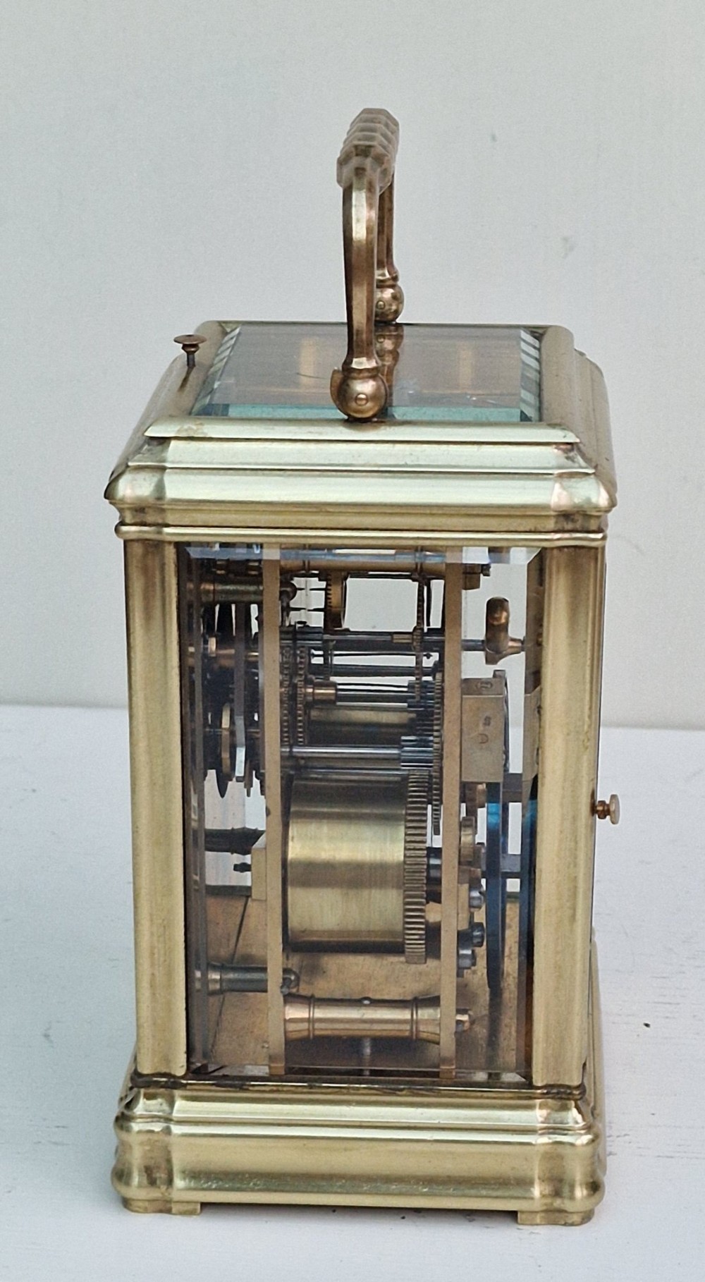 An antique French brass carriage clock featuring a gorge case structure, bevelled glass side panels, a white enamel dial with Roman numerals, and a top carrying handle. View VI