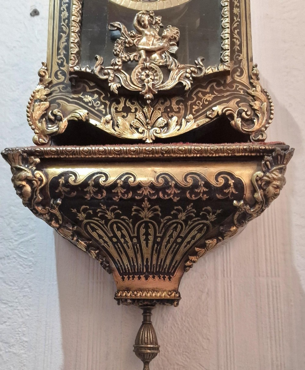 An ornate French Rococo Boulle clock featuring brass marquetry inlays, gilded bronze cherub mounts, individual enamel cartouche numerals, and a matching wall bracket. View II