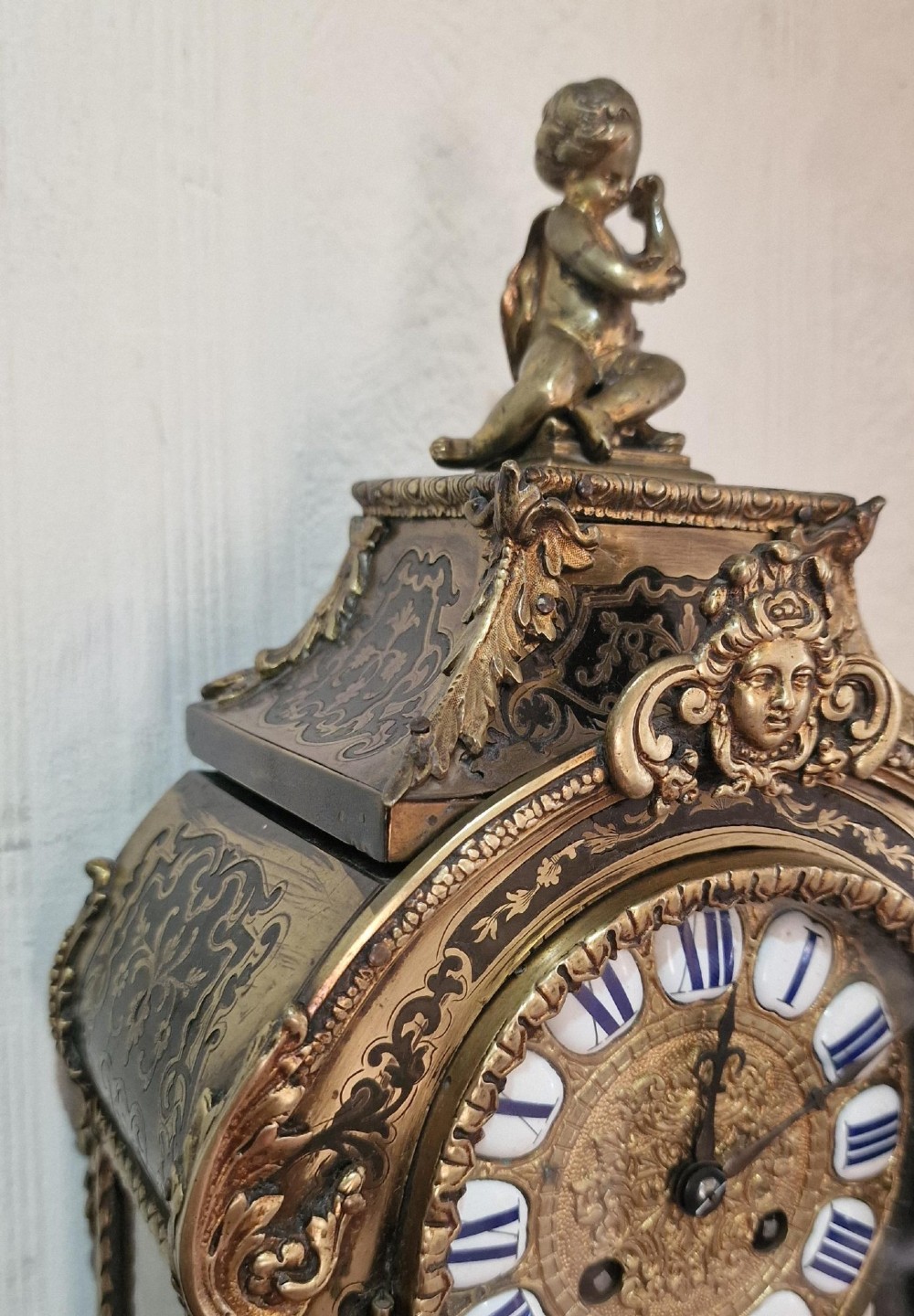 An ornate French Rococo Boulle clock featuring brass marquetry inlays, gilded bronze cherub mounts, individual enamel cartouche numerals, and a matching wall bracket. View III