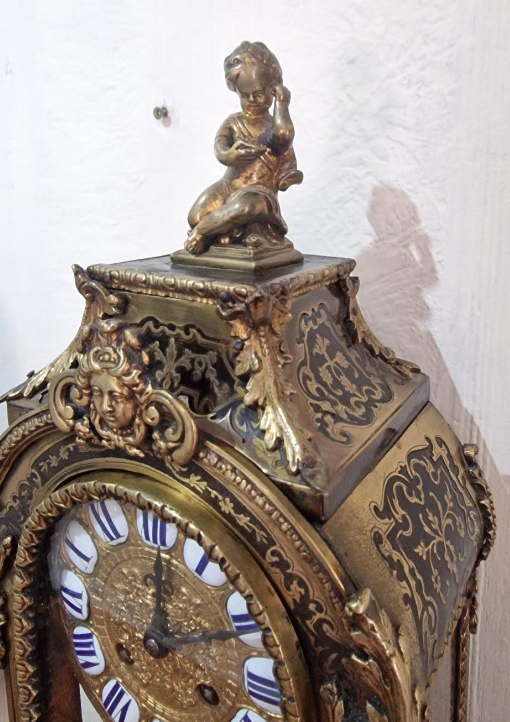 An ornate French Rococo Boulle clock featuring brass marquetry inlays, gilded bronze cherub mounts, individual enamel cartouche numerals, and a matching wall bracket. View IV