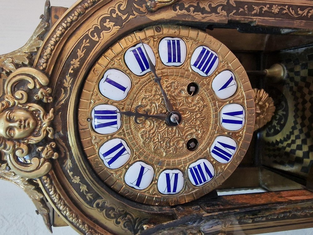 An ornate French Rococo Boulle clock featuring brass marquetry inlays, gilded bronze cherub mounts, individual enamel cartouche numerals, and a matching wall bracket. View V