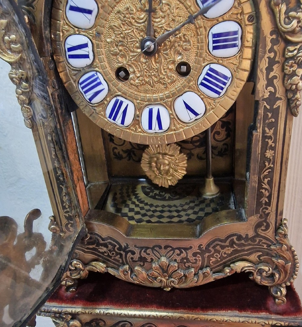 An ornate French Rococo Boulle clock featuring brass marquetry inlays, gilded bronze cherub mounts, individual enamel cartouche numerals, and a matching wall bracket. View VI