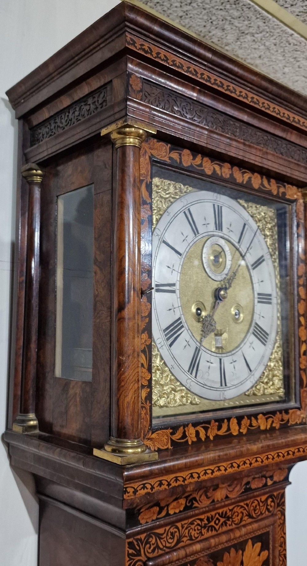 An English late 17th-century longcase clock with intricate floral marquetry veneer, a square brass dial, and a circular glass lenticle on the trunk door. View VI