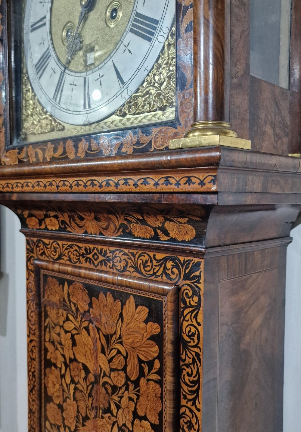 An English late 17th-century longcase clock with intricate floral marquetry veneer, a square brass dial, and a circular glass lenticle on the trunk door. View VIII