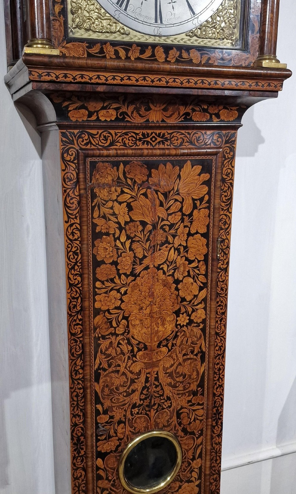 An English late 17th-century longcase clock with intricate floral marquetry veneer, a square brass dial, and a circular glass lenticle on the trunk door. View IX
