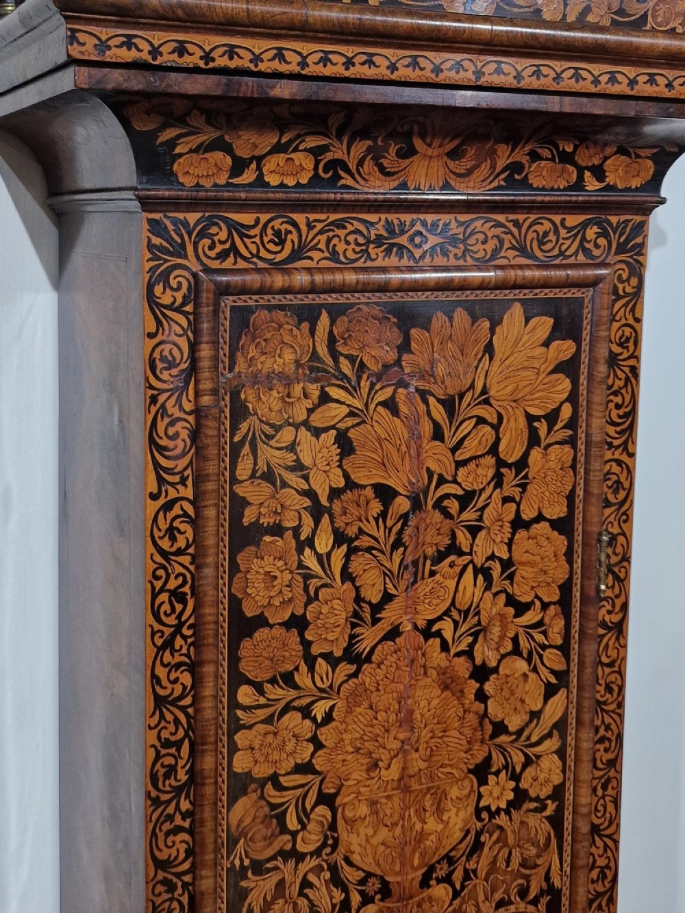 An English late 17th-century longcase clock with intricate floral marquetry veneer, a square brass dial, and a circular glass lenticle on the trunk door. View X