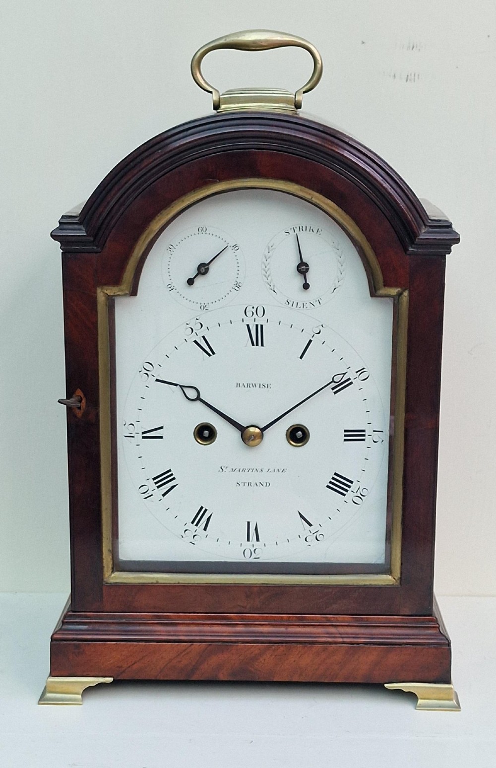 An antique Georgian mahogany bracket clock featuring an arched top with a brass carrying handle, brass bracket feet, and a white dial inscribed Barwise London.