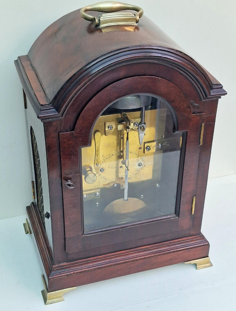 An antique Georgian mahogany bracket clock featuring an arched top with a brass carrying handle, brass bracket feet, and a white dial inscribed Barwise London. View II