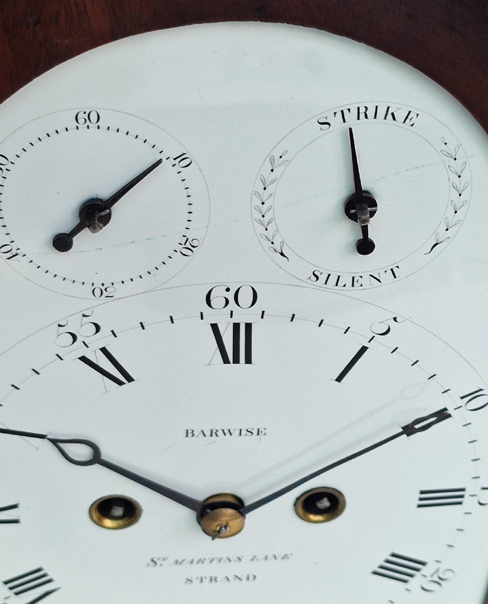 An antique Georgian mahogany bracket clock featuring an arched top with a brass carrying handle, brass bracket feet, and a white dial inscribed Barwise London. View III