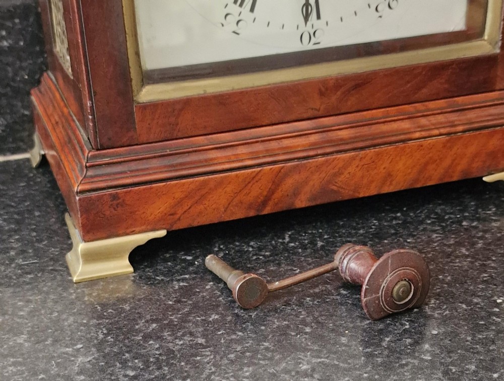 An antique Georgian mahogany bracket clock featuring an arched top with a brass carrying handle, brass bracket feet, and a white dial inscribed Barwise London. View IV