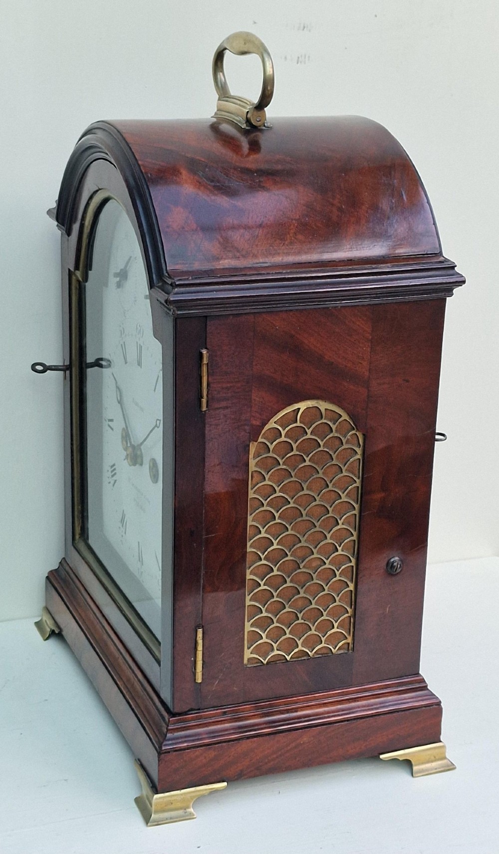 An antique Georgian mahogany bracket clock featuring an arched top with a brass carrying handle, brass bracket feet, and a white dial inscribed Barwise London. View VII