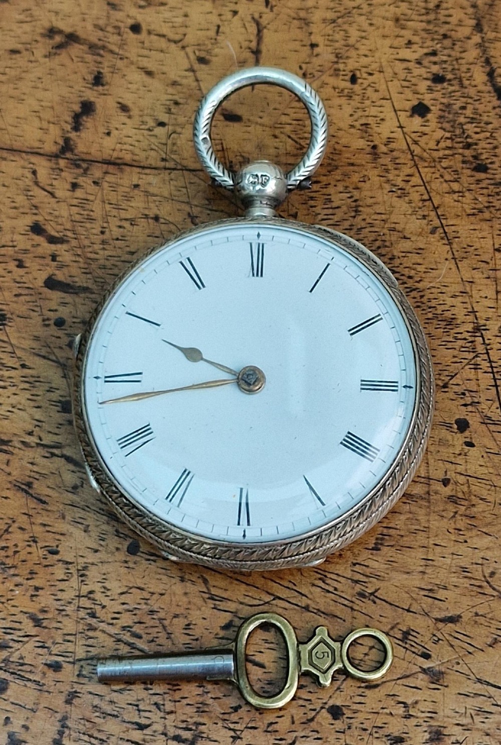 A Victorian silver open-face pocket watch featuring a white enamel dial with Roman numerals alongside an accompanying brass winding key.