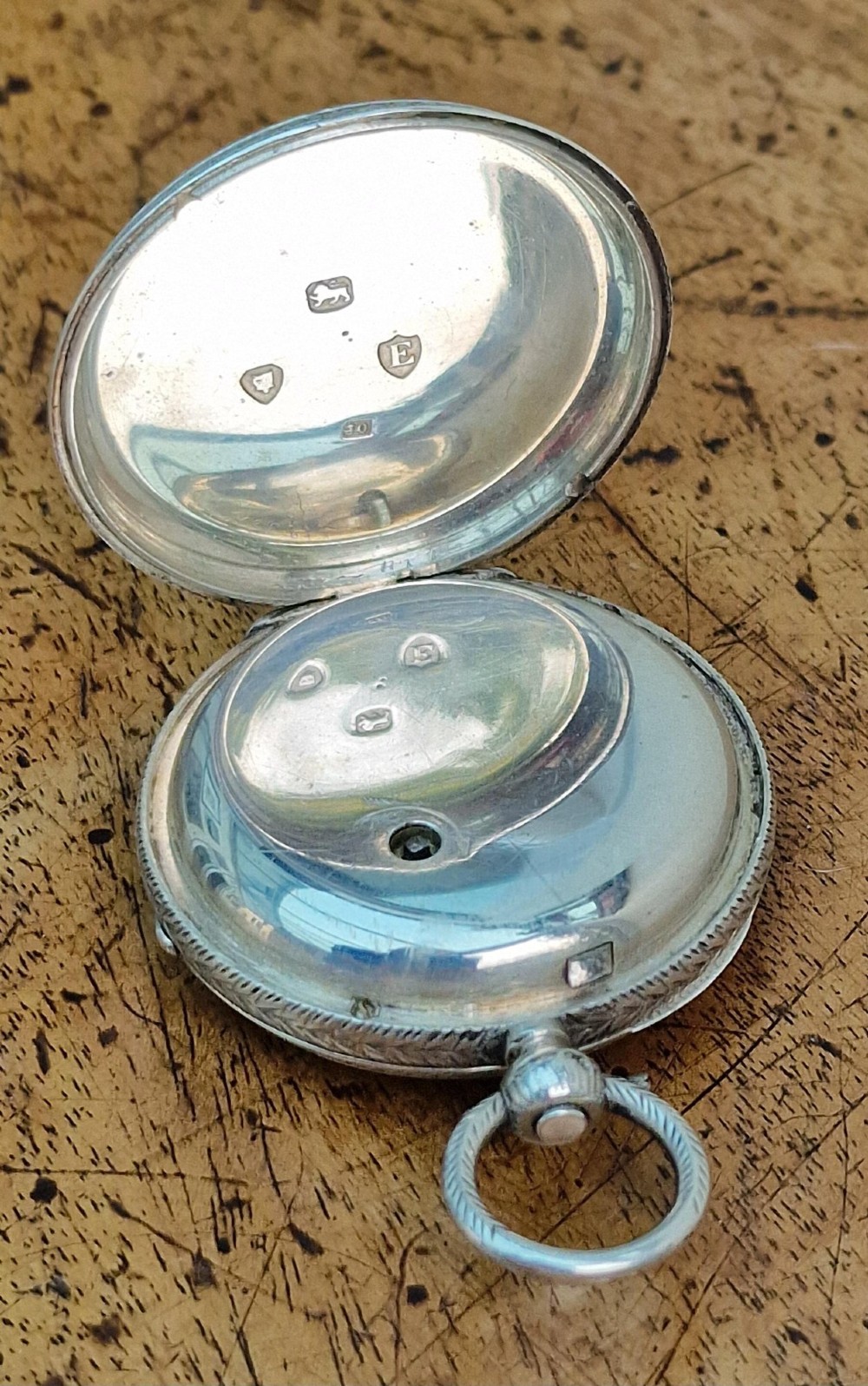 A Victorian silver open-face pocket watch featuring a white enamel dial with Roman numerals alongside an accompanying brass winding key. View V
