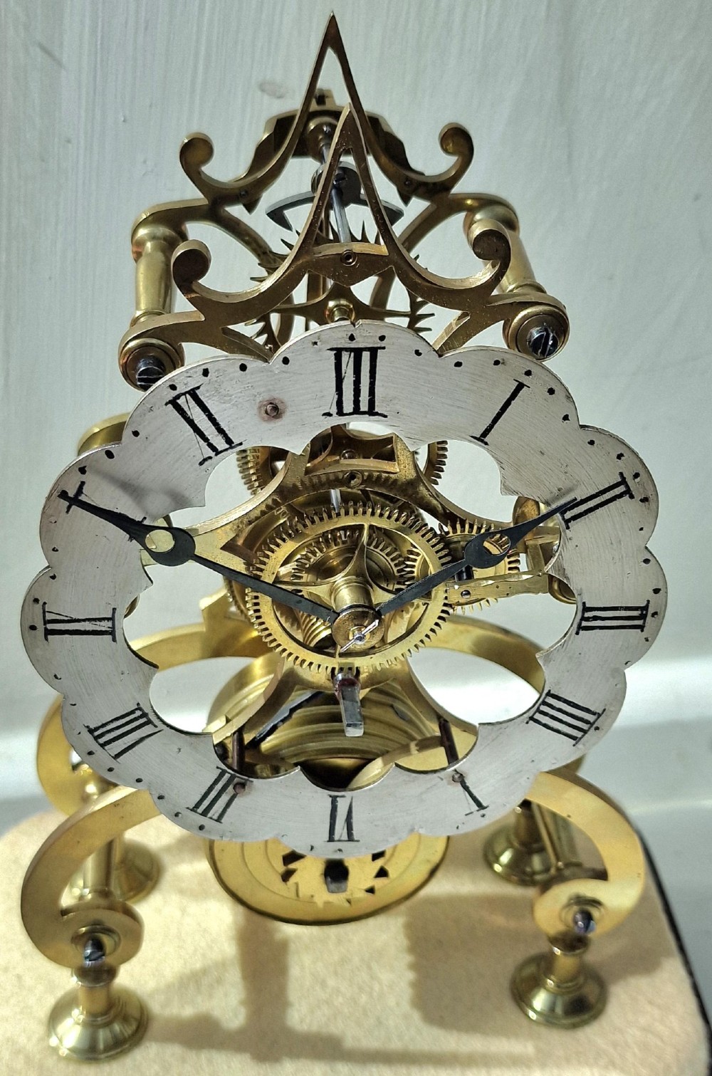 A Victorian brass skeleton clock displaying exposed gearwork and a silvered chapter ring with Roman numerals, set on a plinth under a clear glass dome. View II