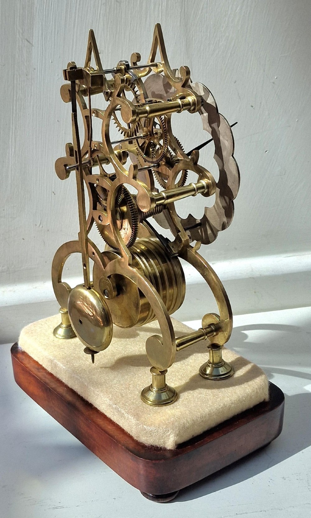 A Victorian brass skeleton clock displaying exposed gearwork and a silvered chapter ring with Roman numerals, set on a plinth under a clear glass dome. View V