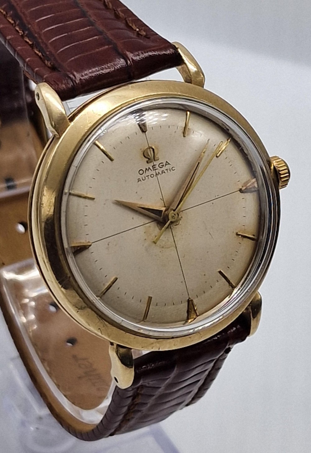 A 1950s vintage Omega automatic wristwatch crafted with a 9K gold case and brown leather strap, set inside a red presentation box. View VI