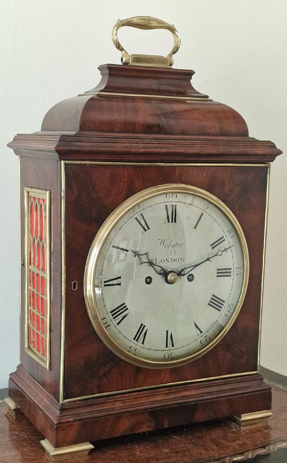 A Georgian flame mahogany bracket clock featuring a brass carrying handle, circular white dial with Roman numerals, and brass-backed side frets.