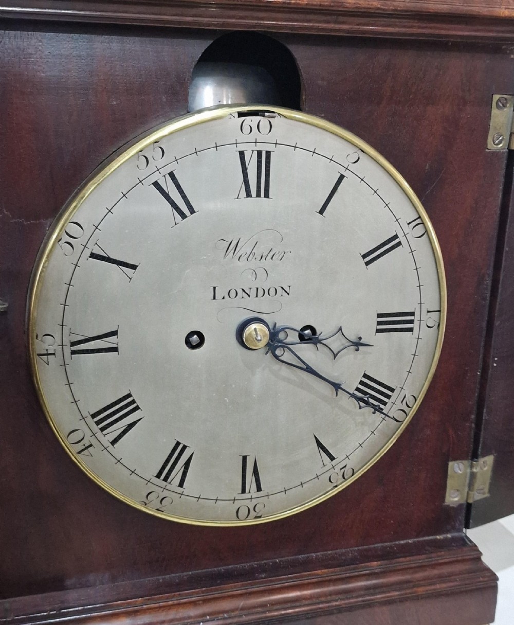 A Georgian flame mahogany bracket clock featuring a brass carrying handle, circular white dial with Roman numerals, and brass-backed side frets. View VI