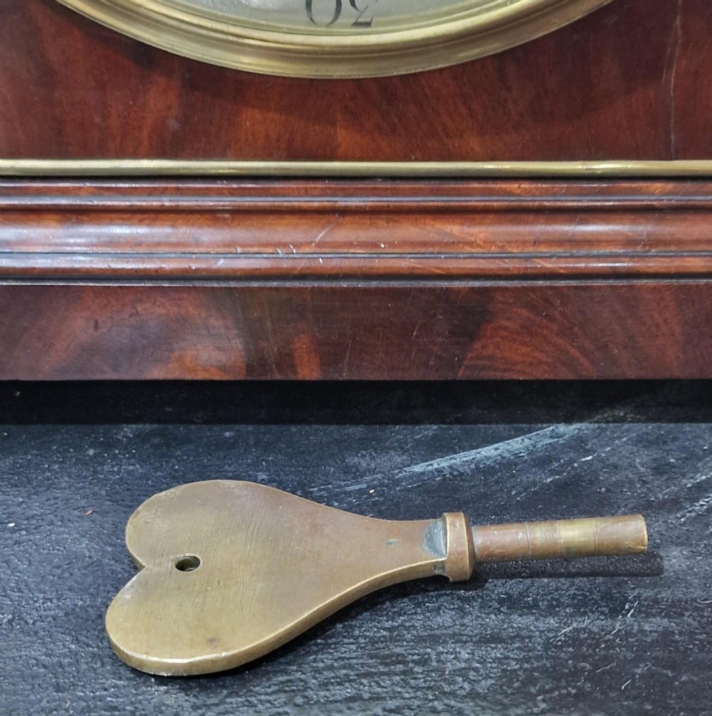 A Georgian flame mahogany bracket clock featuring a brass carrying handle, circular white dial with Roman numerals, and brass-backed side frets. View VII