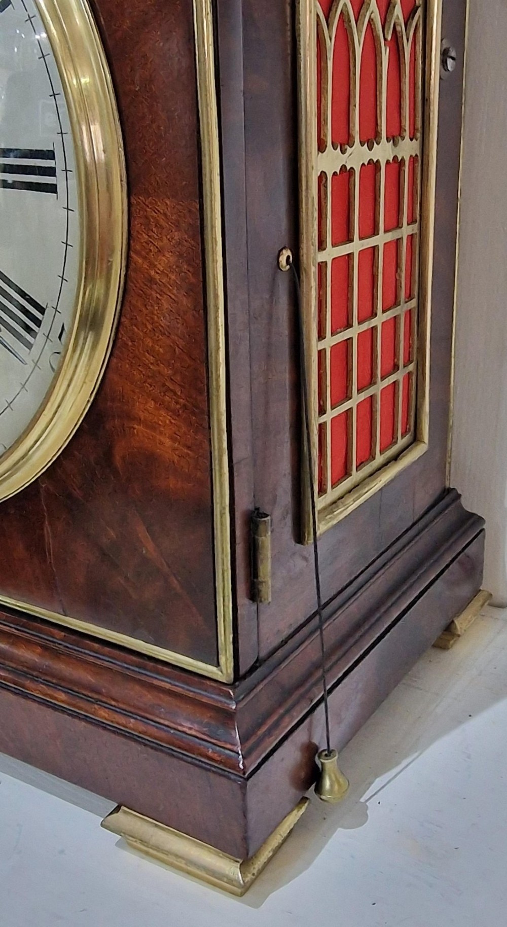 A Georgian flame mahogany bracket clock featuring a brass carrying handle, circular white dial with Roman numerals, and brass-backed side frets. View IX