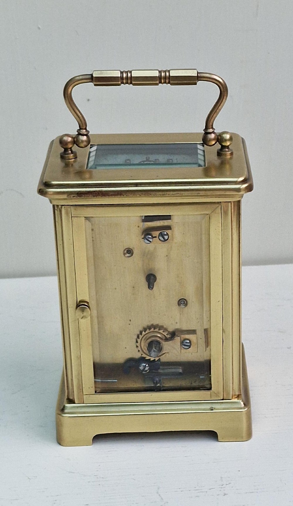 An antique French brass carriage clock featuring bevelled glass panels, a white enamel dial with black Roman numerals, and a top carrying handle. View II